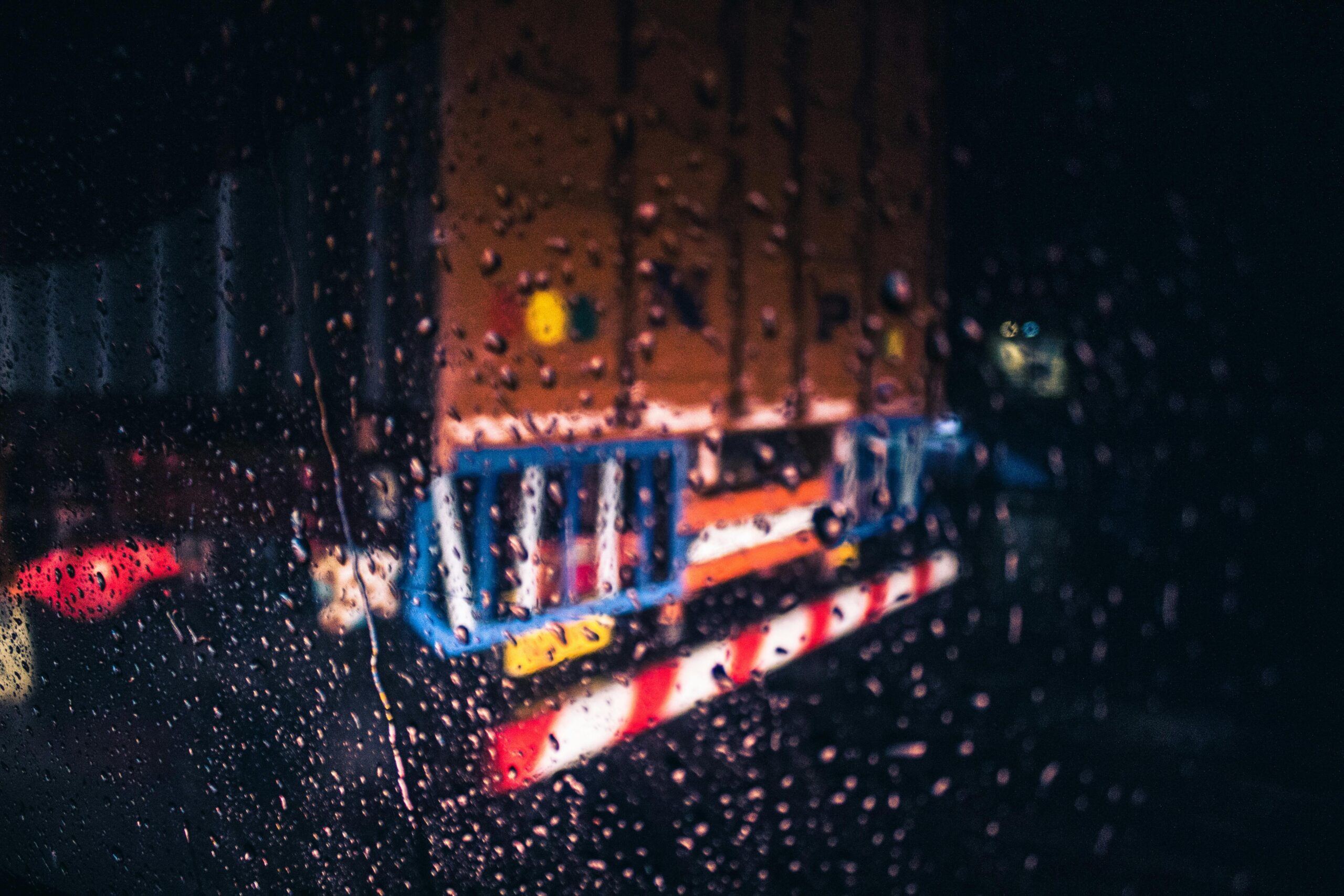 Blurred view of a truck through a rainy window at night, with water droplets on glass.